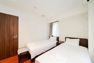 a hotel room with two beds and a chair at Serorin Light Hotel Tokyo in Tokyo