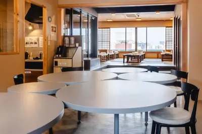 a cafeteria with white tables and chairs and a kitchen at COGO Ryogoku in Tokyo