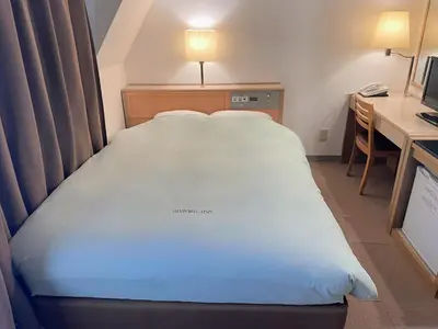 a large bed in a hotel room with a desk and a desk at Olympic Inn Kanda in Tokyo