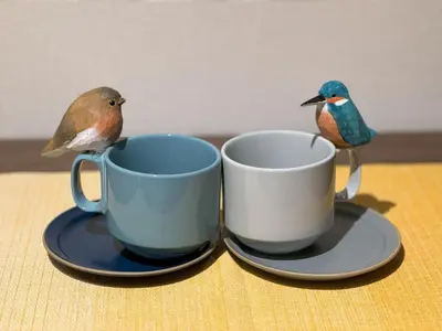 two birds perched on two coffee cups on a table at nestay apartment tokyo shinjuku in Tokyo