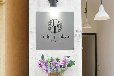 a sign on a wall with purple flowers in a vase at Hostel Lodging Tokyo Ueno in Tokyo