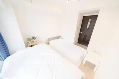 a bedroom with a bed with white sheets and a door at Square Shibuya in Tokyo