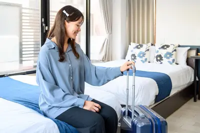 a woman sitting on a bed with a suitcase at Ueno Woo Hotel in Tokyo